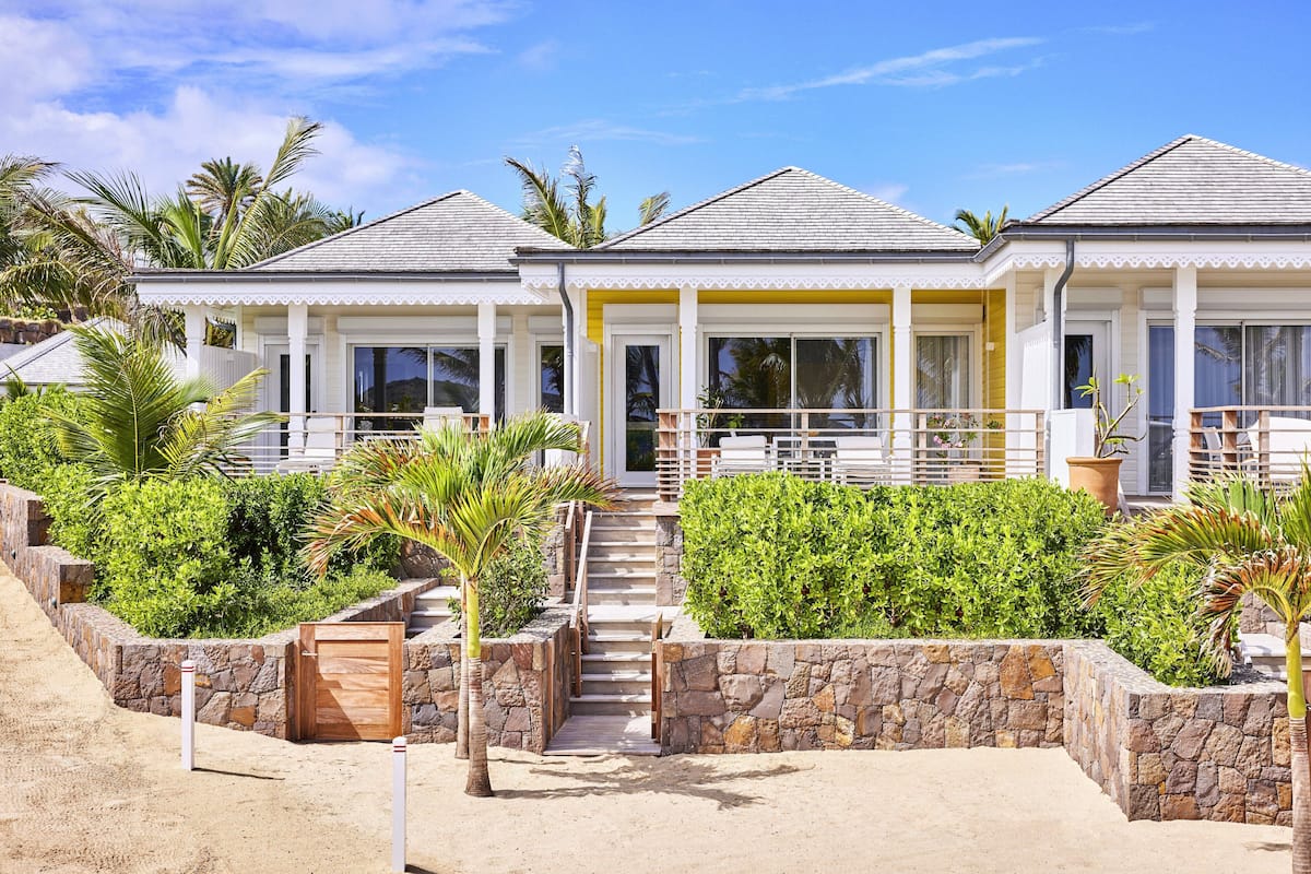 A beachfront property with a stone retaining wall, a wooden staircase, and a covered porch.