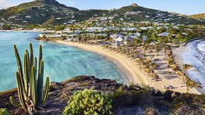 A coastal resort with a beach, palm trees, and a mountain in the background. - Rosewood Le Guanahani St Barth (St. Barthelemy)