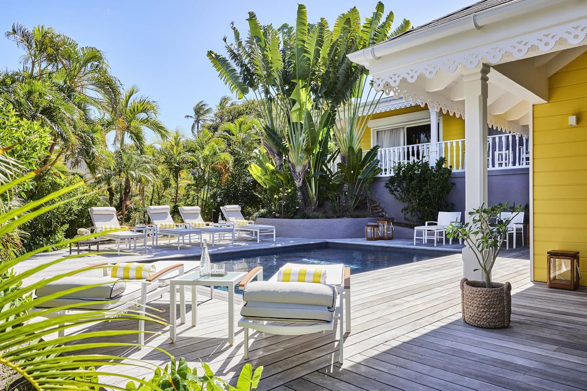 A poolside area with lounge chairs and a small table, surrounded by tropical plants.