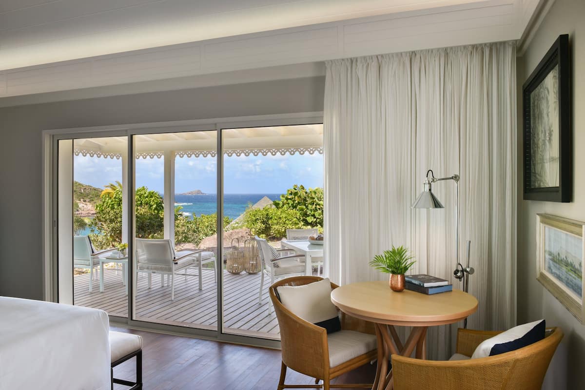 A room with a large sliding glass door leading to an outdoor deck with a view of the ocean. There is a round table with chairs and a potted plant.