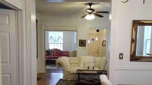 A spacious living room with a wooden floor, a dining area with a table and chairs, and a ceiling fan.