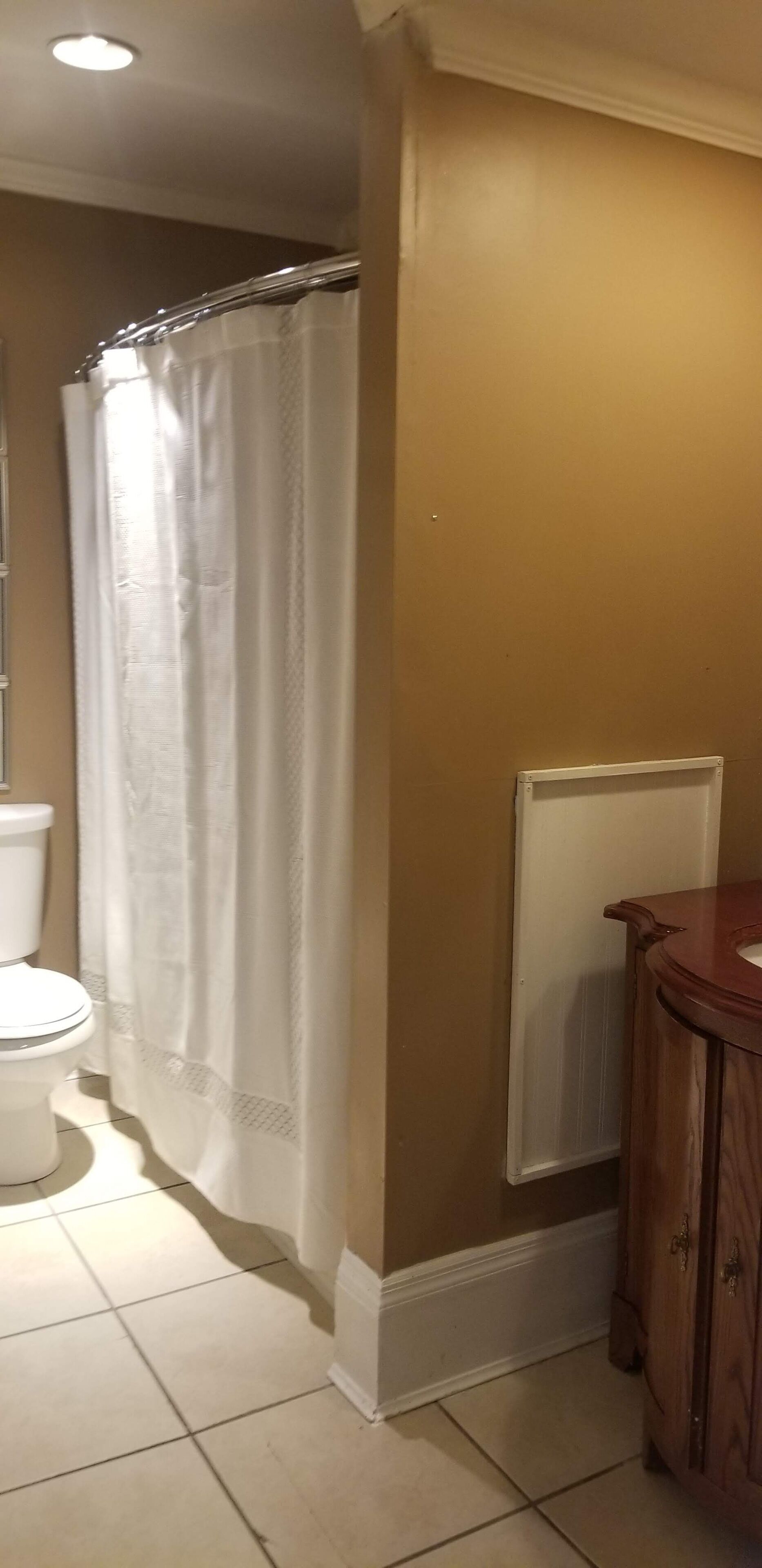 Un baño con inodoro, cortina de ducha, radiador y armarios de madera.