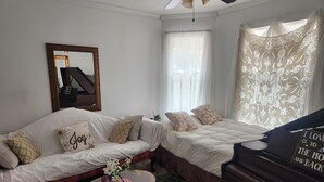 A cozy room with a sofa, a piano, a mirror, and a window with sheer curtains.