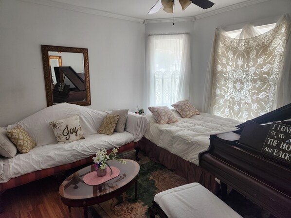 A cozy room with a sofa, a piano, a mirror, and a window with sheer curtains.