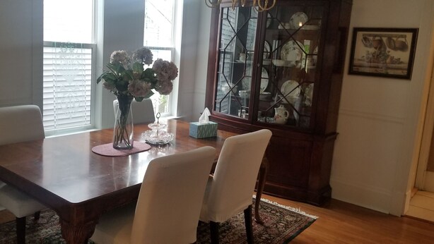 A dining area with a wooden table, white chairs, a vase with flowers, and a china cabinet.
