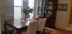 A dining area with a wooden table, white chairs, a vase with flowers, and a china cabinet.