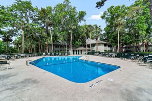 A swimming pool with a diving board, surrounded by lounge chairs and tall trees.