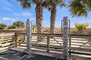 A gated entrance with a wooden fence and metal gates, palm trees in the background, and a clear sky.