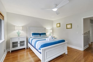 A bedroom with a bed, bedside tables, a ceiling fan, and a door leading to another room.