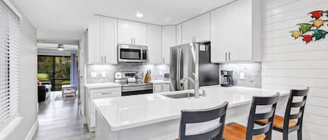 Una cocina moderna con armarios blancos, electrodomésticos de acero inoxidable y una isla central con taburetes de bar.