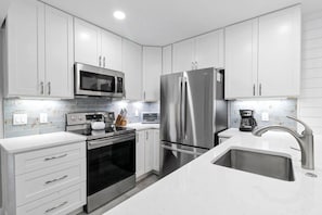 A modern kitchen with stainless steel appliances, white cabinetry, and a white countertop.