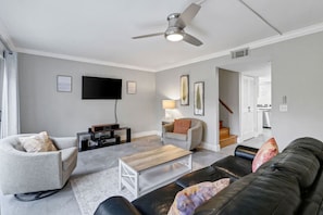 A living room with a flat-screen TV, a ceiling fan, and a staircase leading to an upper floor.