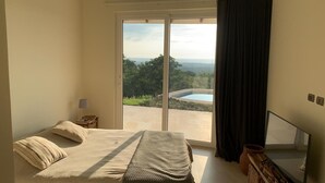 A bedroom with a bed, a nightstand, a lamp, and a view of a swimming pool and greenery through a sliding door. - House with terrace and pool. (Playa Negra Finca Los Pargos)