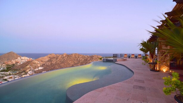 A pool with a curved edge, a stone building with a thatched roof, and a view of a coastal town. - Luxury Pacific View Villa, Cabo San Lucas Villa 1005 (Cabo San Lucas)