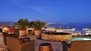 A terrace with wicker chairs, potted plants, and a stone fire pit overlooking a coastal cityscape at night. - Luxury Pacific View Villa, Cabo San Lucas Villa 1005 (Cabo San Lucas)