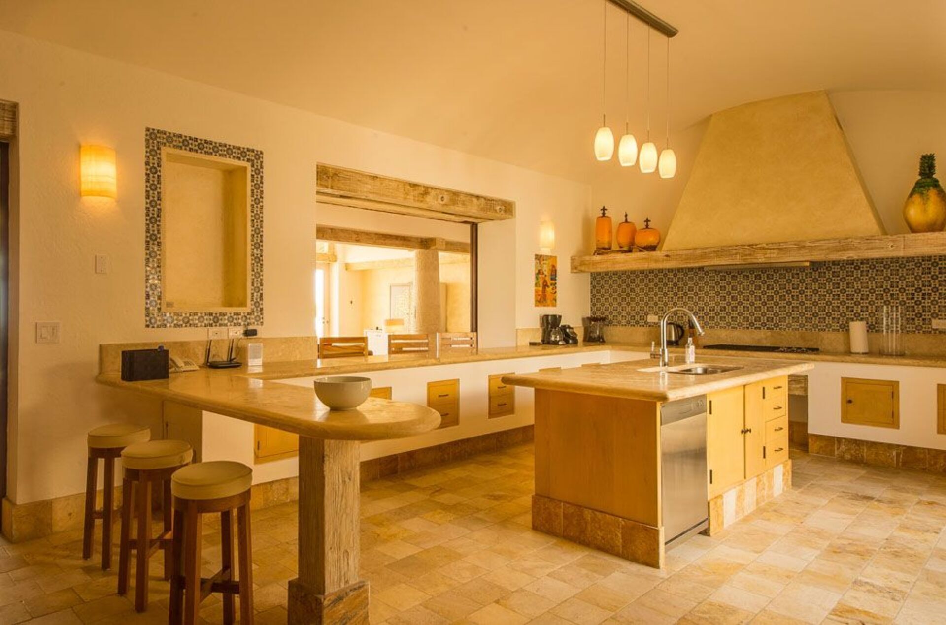 A spacious kitchen with a large island, wooden stools, and a hanging light fixture.