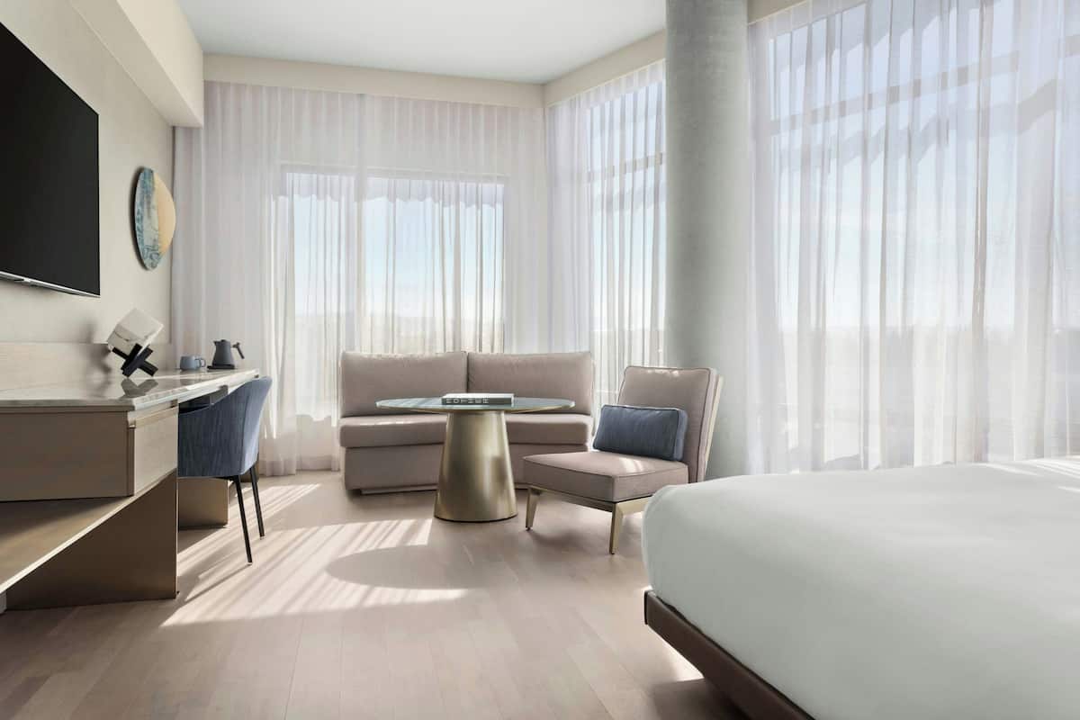 A modern hotel room with a bed, a desk, a sofa, and a coffee table.