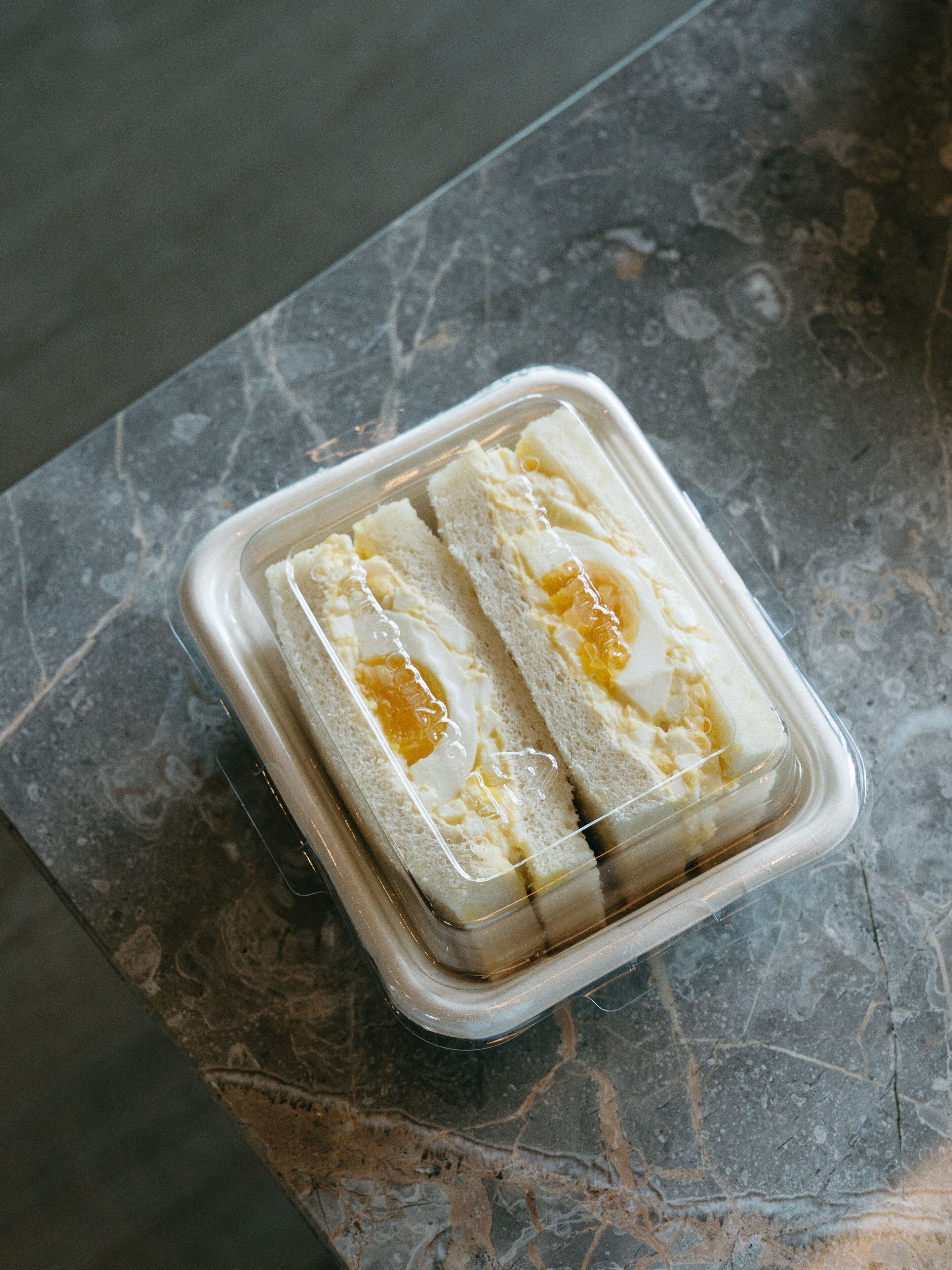 A clear plastic container with two slices of white bread and a spread on a marble surface.