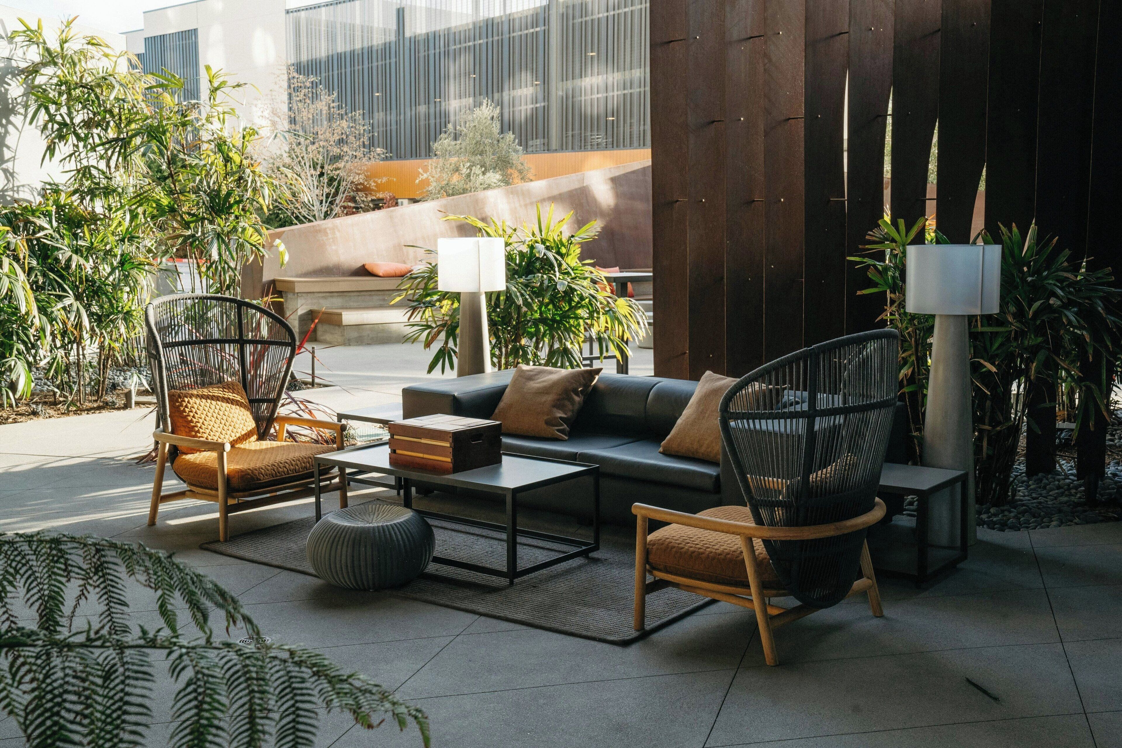 An outdoor seating area with modern furniture, including a sofa, chairs, and a coffee table. There are potted plants and a lamp post.