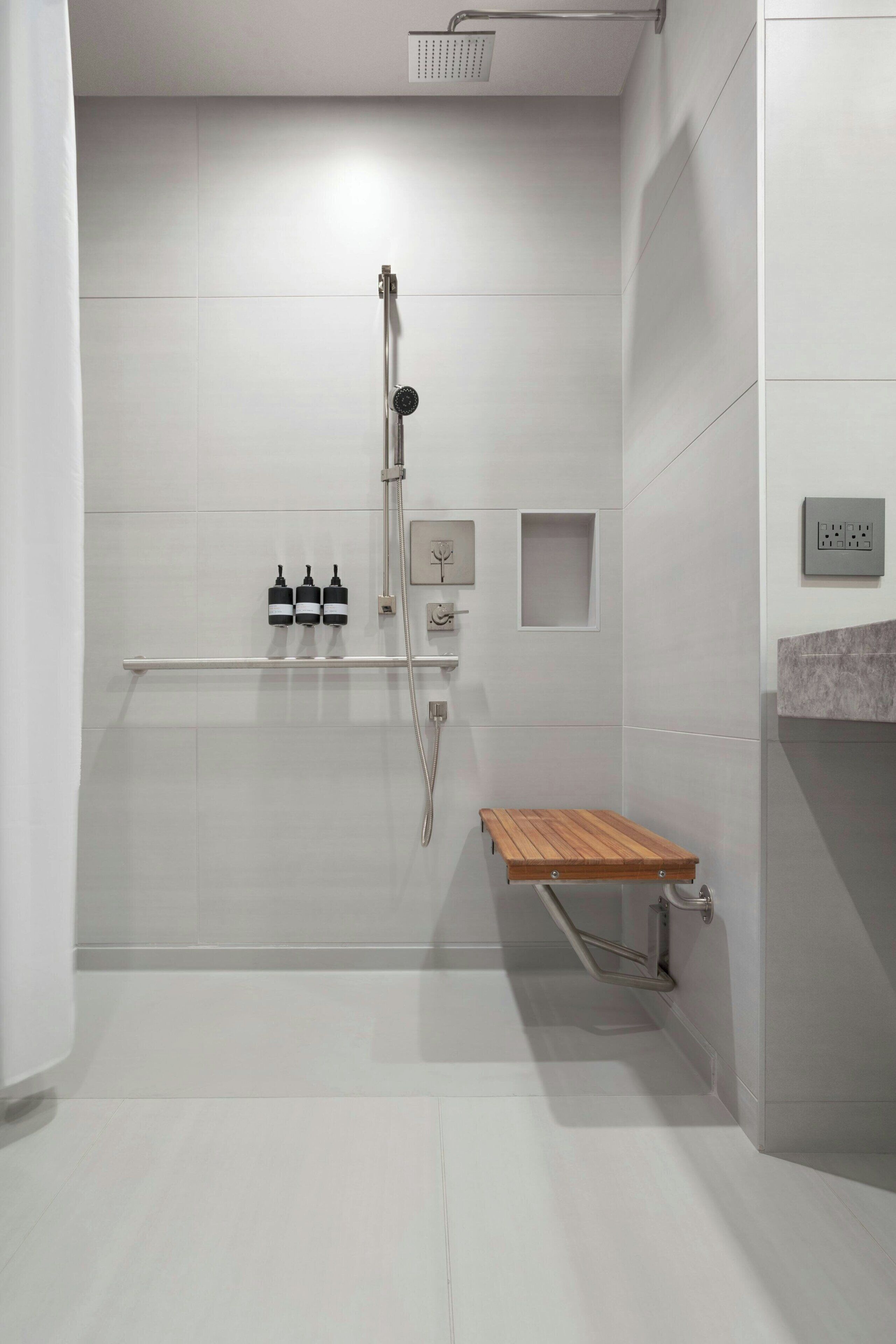 A modern bathroom with a shower, a wooden bench, and a shelf with toiletries.