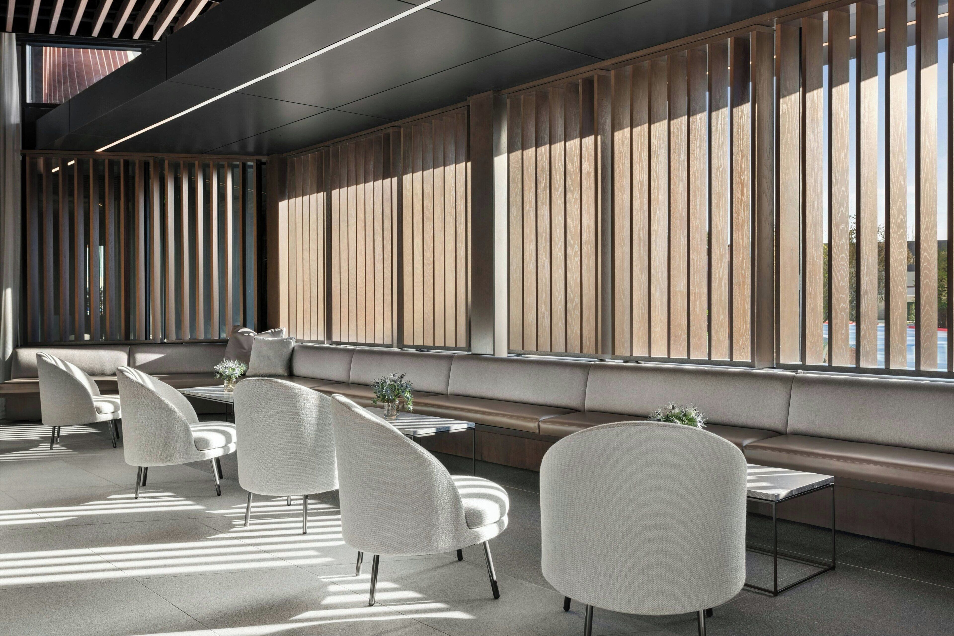 A modern interior with a seating area, tables, and a large window with vertical blinds.
