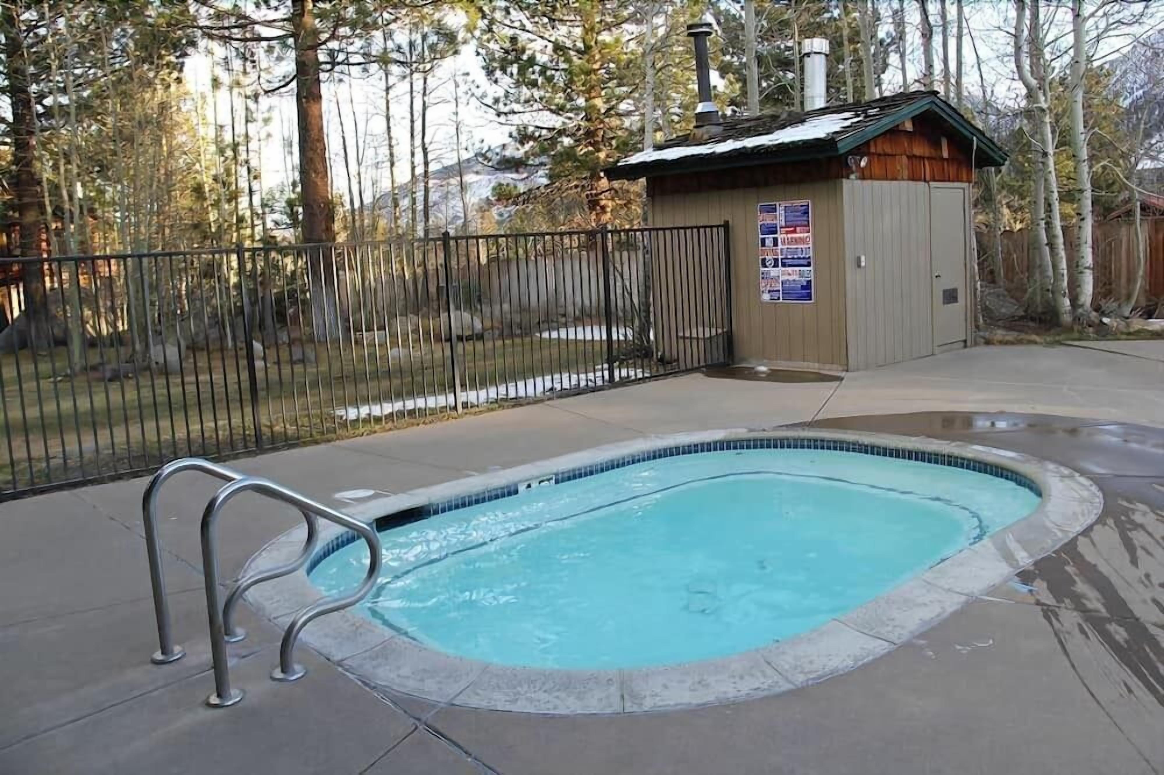 A small outdoor swimming pool with a metal ladder, surrounded by a fence and a wooden structure with a chimney.