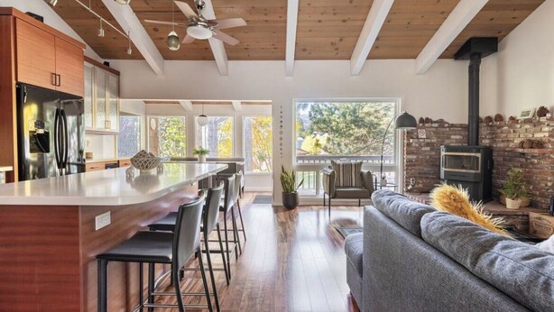 A modern kitchen with a central island, wooden ceiling beams, and a stone fireplace.