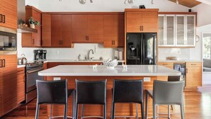 A modern kitchen with wooden cabinets, a central island, and bar stools.