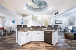 A spacious kitchen with a large island, white cabinetry, and a modern staircase.