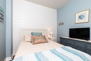 Een slaapkamer met een bed, een televisie, een nachtkastje en een muur met een ingelijst schilderij.