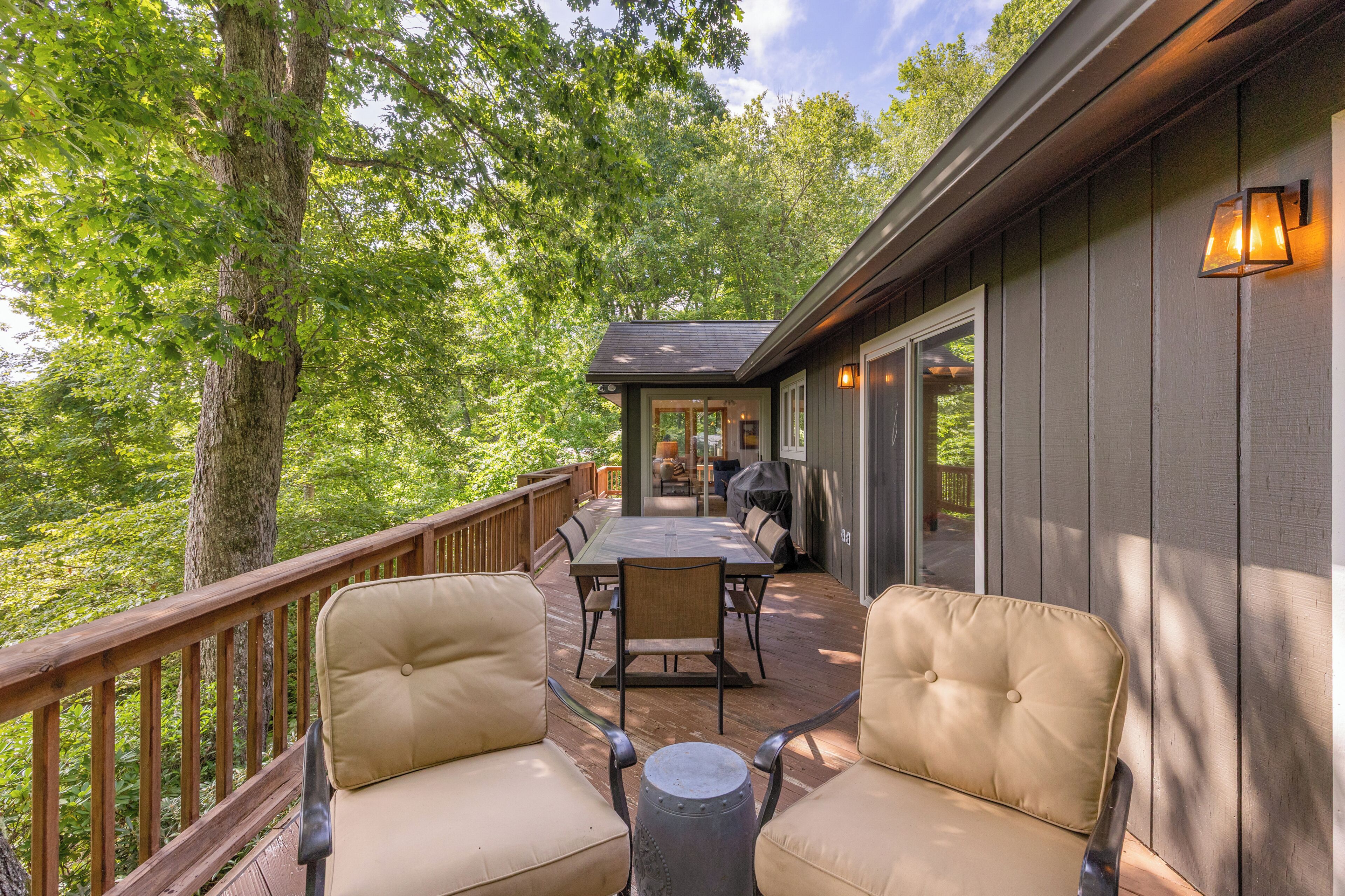 Une terrasse dotée de mobilier d’extérieur, d’un barbecue couvert et offrant une vue sur la forêt environnante.