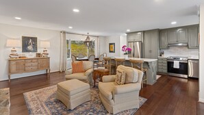 A spacious living room with a large rug, a dining area with chairs, a kitchen with modern appliances, and a view through a glass door. - Charming newly renovated cottage, incredible mountain views, walk to town (Highlands)