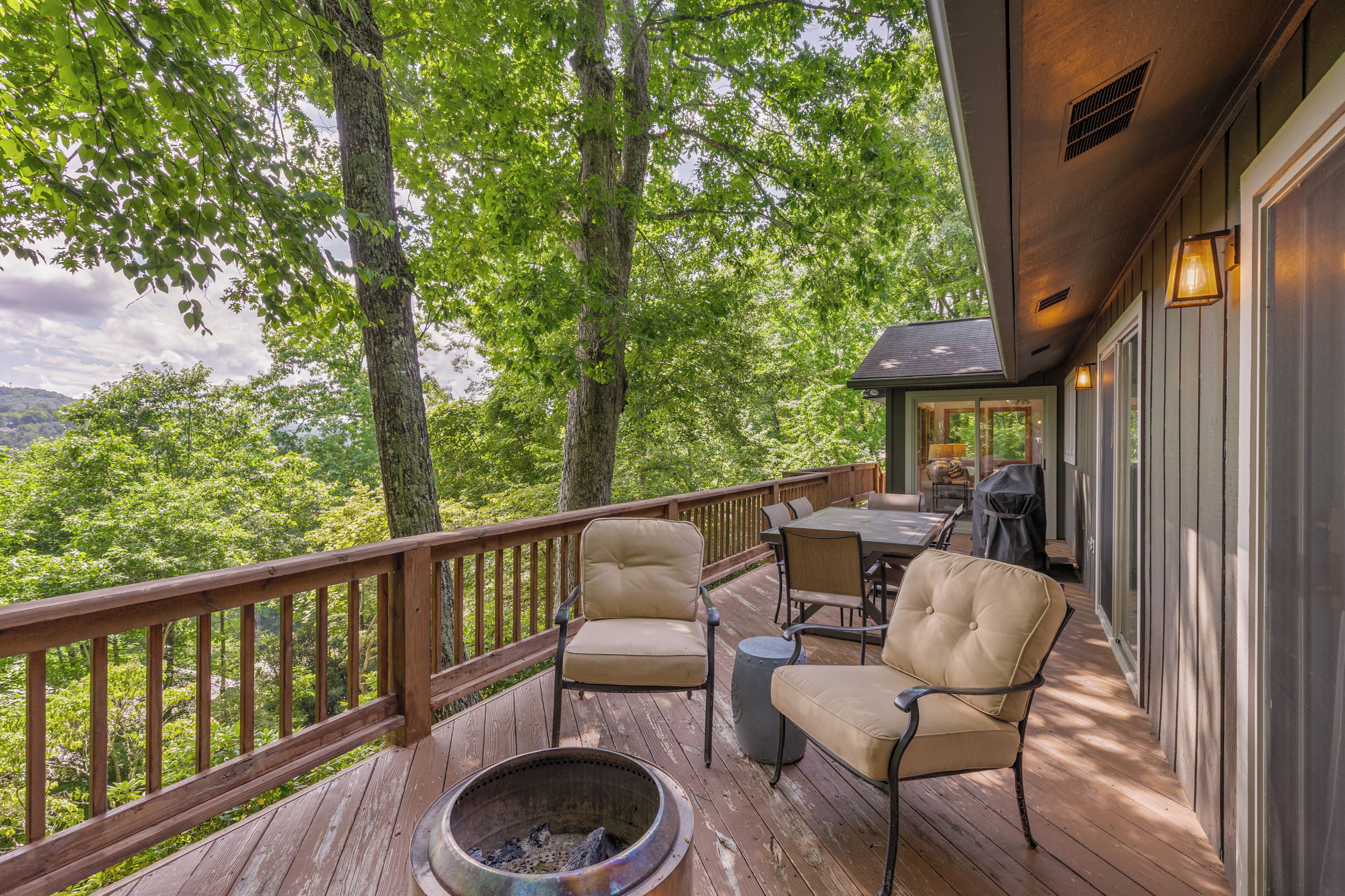 A wooden deck with outdoor furniture, a fire pit, and a view of a forested landscape.