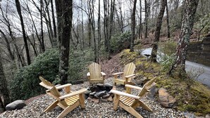 A forested area with a fire pit and four wooden Adirondack chairs. - Charming newly renovated cottage, incredible mountain views, walk to town (Highlands)