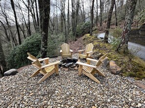 A forested area with a fire pit and four wooden Adirondack chairs. - Charming newly renovated cottage, incredible mountain views, walk to town (Highlands)