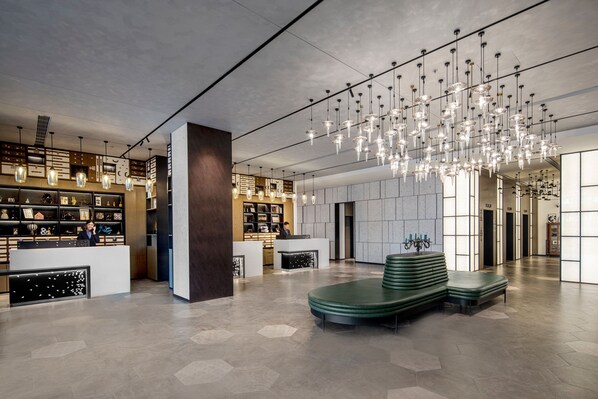 Un hall d’hôtel moderne doté d’un espace salon central, d’un comptoir d’accueil et d’un grand lustre.