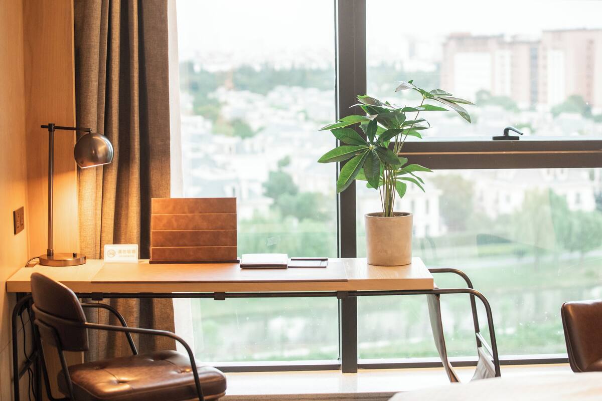 Ein moderner Arbeitsraum mit Schreibtisch, Stühlen, einer Zimmerpflanze und Blick auf eine Skyline durch große Fenster.