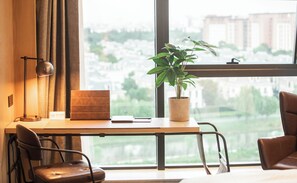 Un espace de bureau moderne comprenant un bureau, des chaises, une plante en pot et une vue sur le paysage urbain, visible à travers de grandes fenêtres.