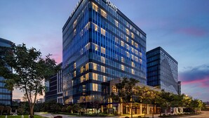 Een modern hotelgebouw met een glazen gevel, meerdere verdiepingen en een opvallend borduur aan de bovenkant.