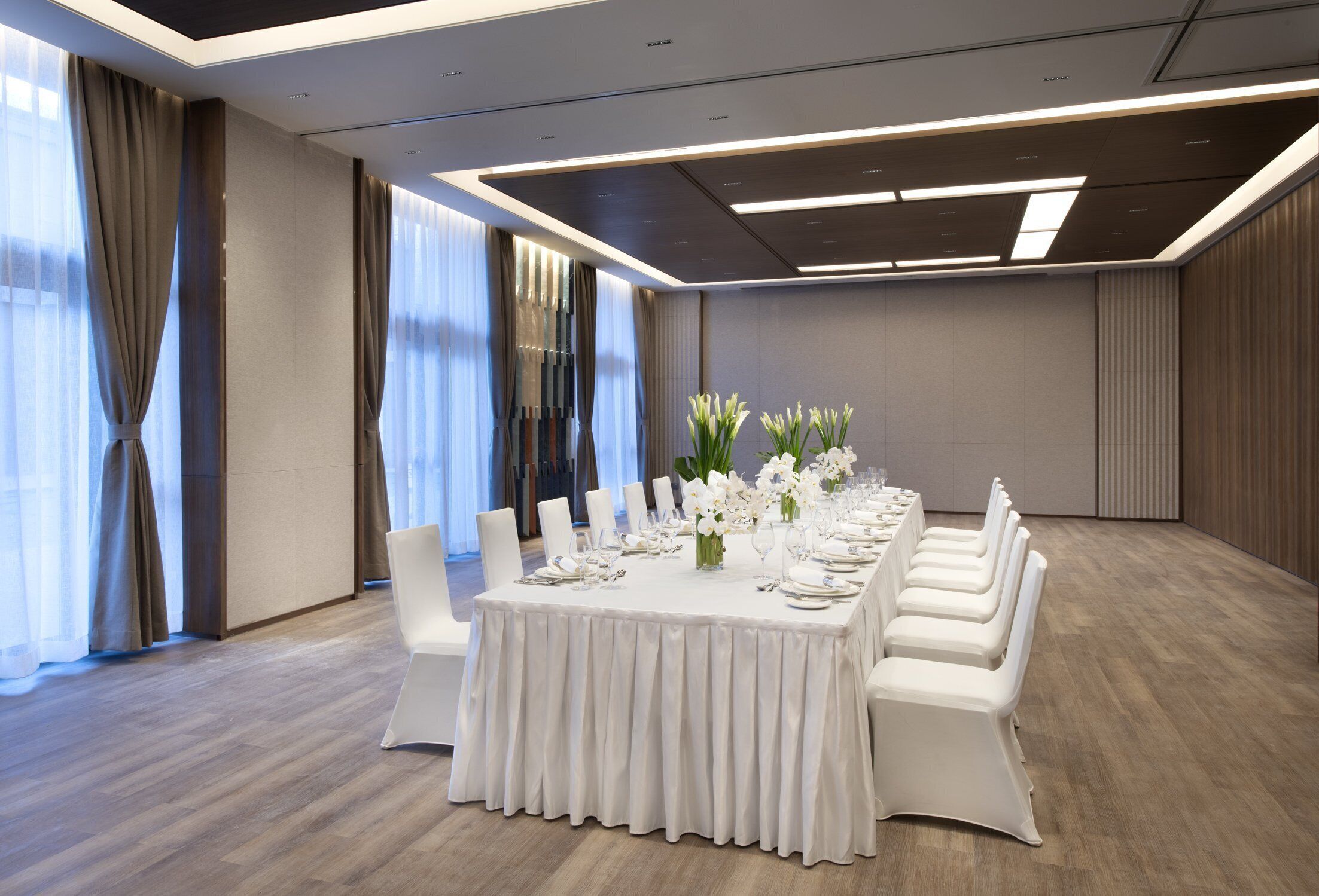 A conference room with a long table set for a meeting, white chairs, and a modern ceiling design.