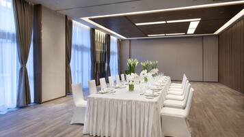 Un salón de conferencias con una larga mesa dispuesta para una reunión, sillas blancas y un diseño de techo moderno.