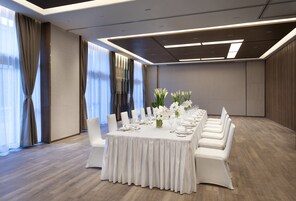 Un salón de conferencias con una larga mesa dispuesta para una reunión, sillas blancas y un diseño de techo moderno.