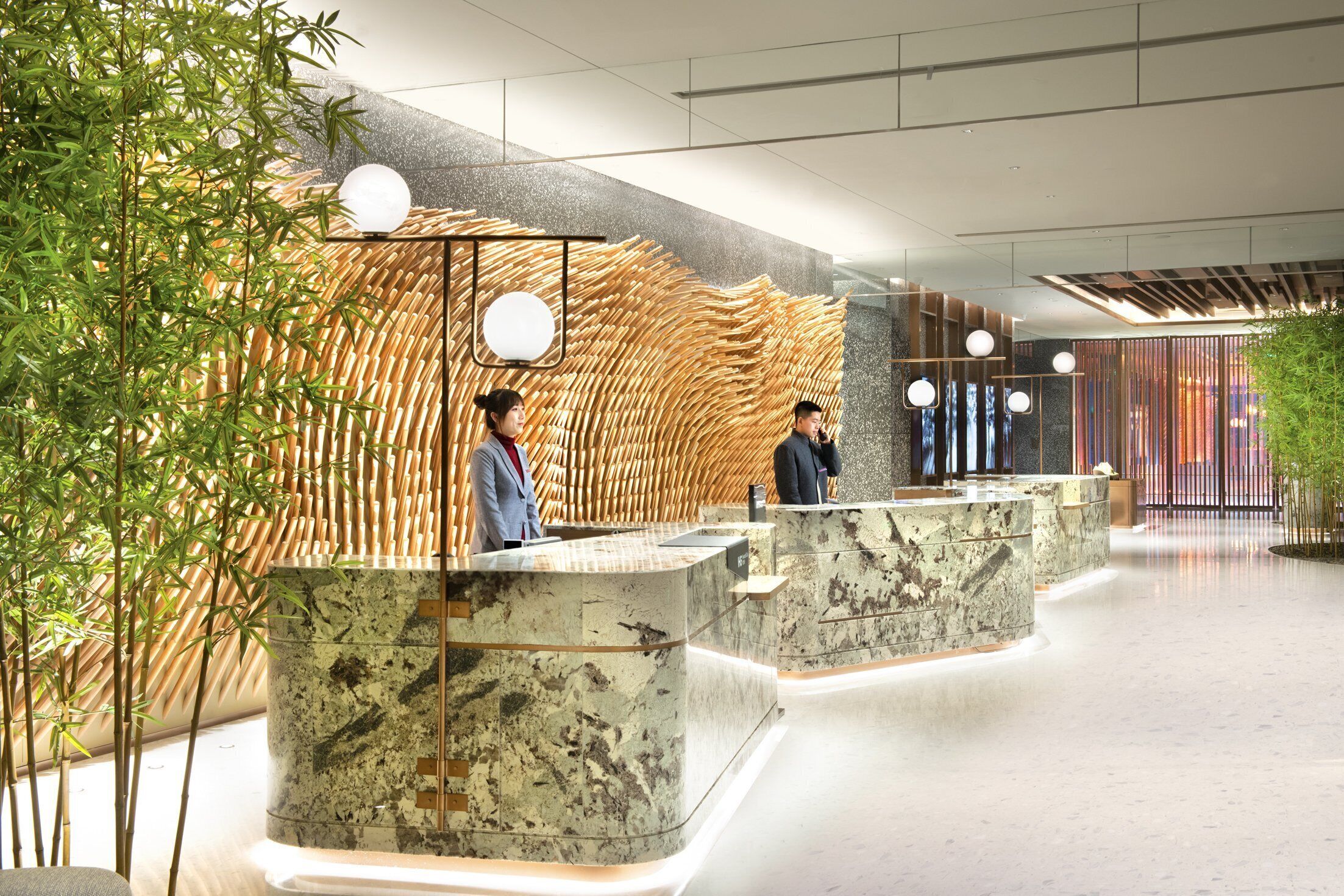 A modern reception area with a bamboo wall, marble counters, and a glass partition.