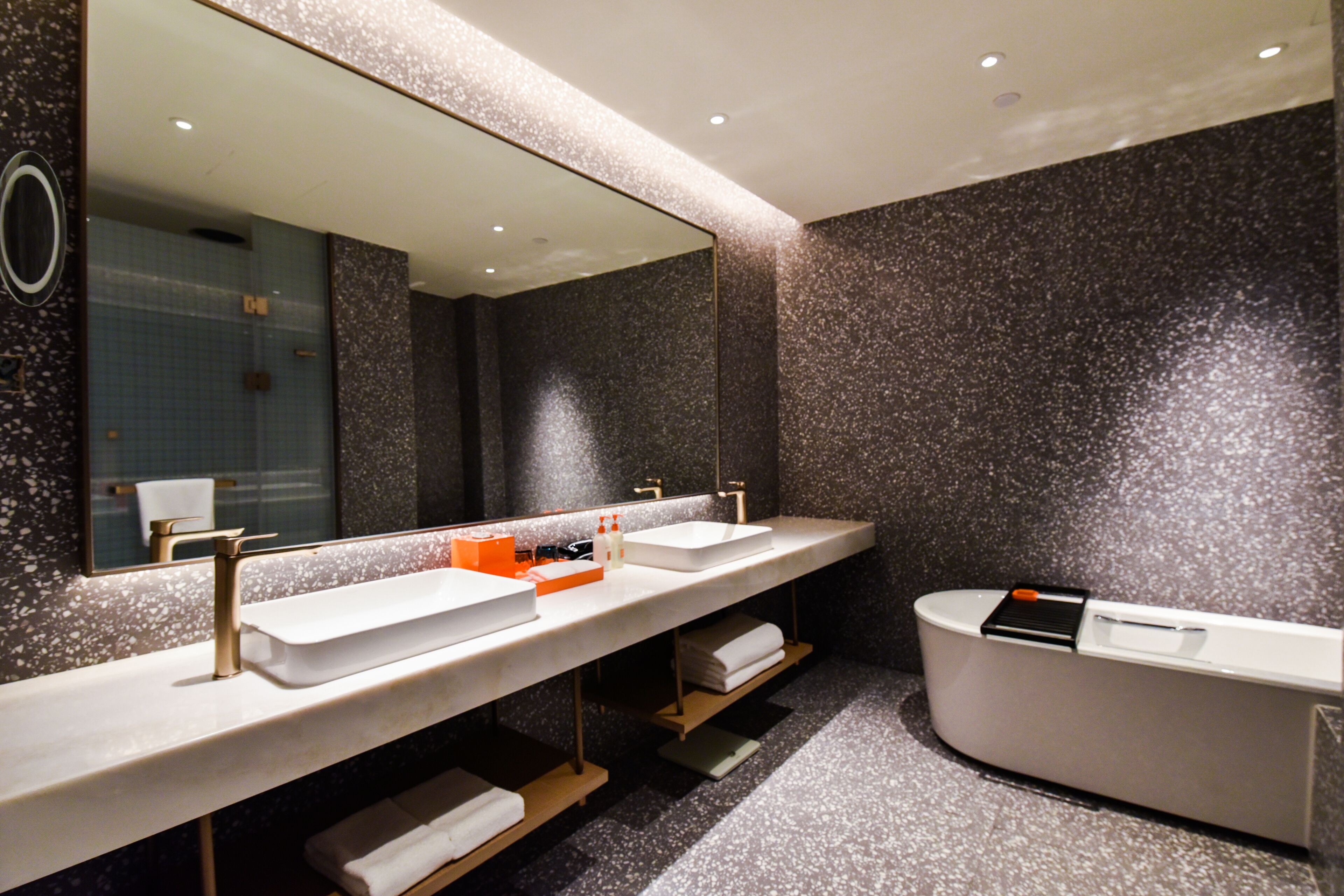 Un baño moderno con un espejo grande, dos lavamanos, una bañera y un perchero para toallas.