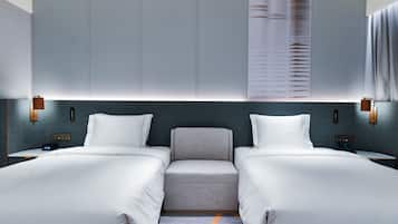 Quarto de hotel com duas camas, um espaço de estar pequeno e uma janela grande com persianas.