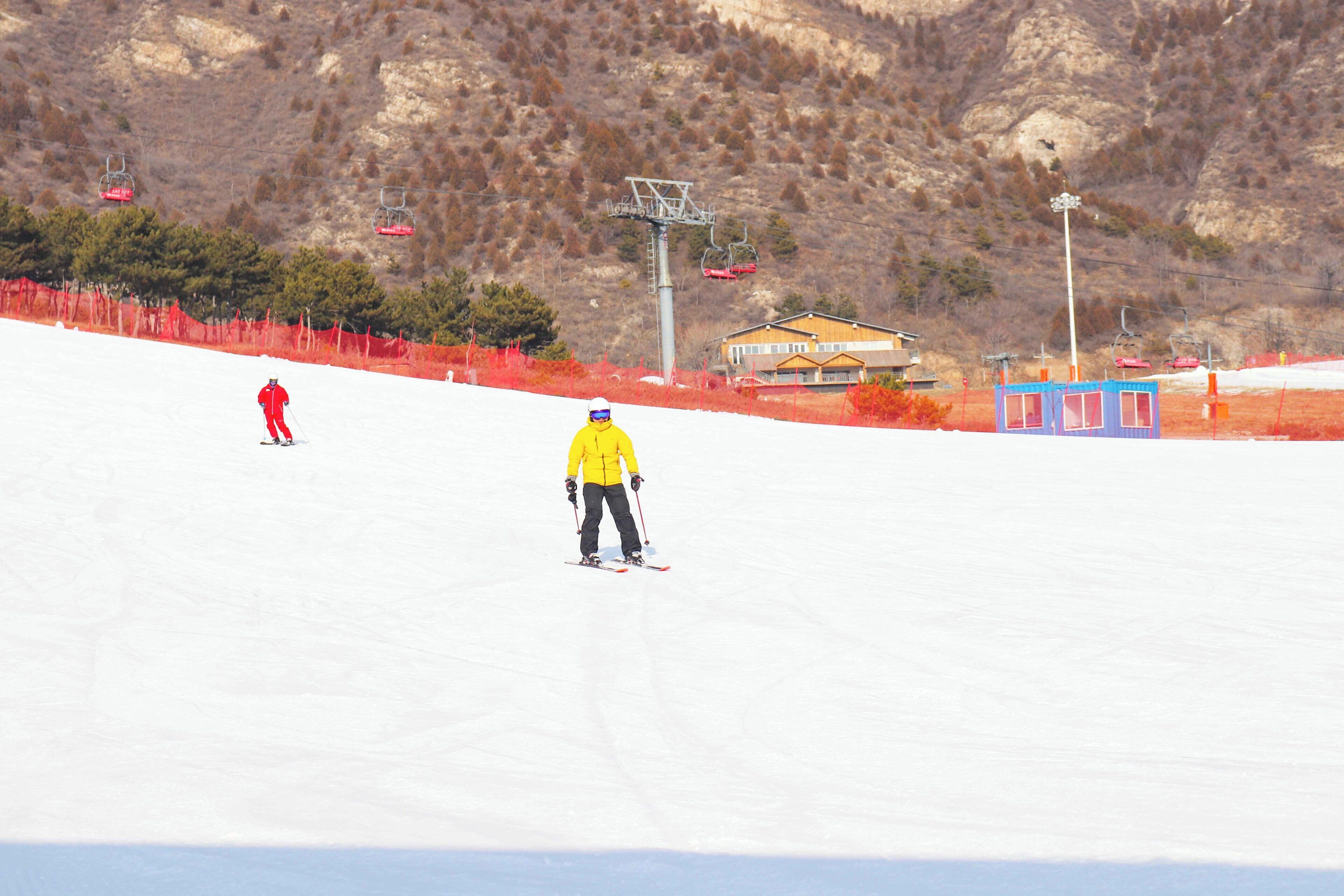 A ski slope with a person skiing, a ski lift, and a building in the background.