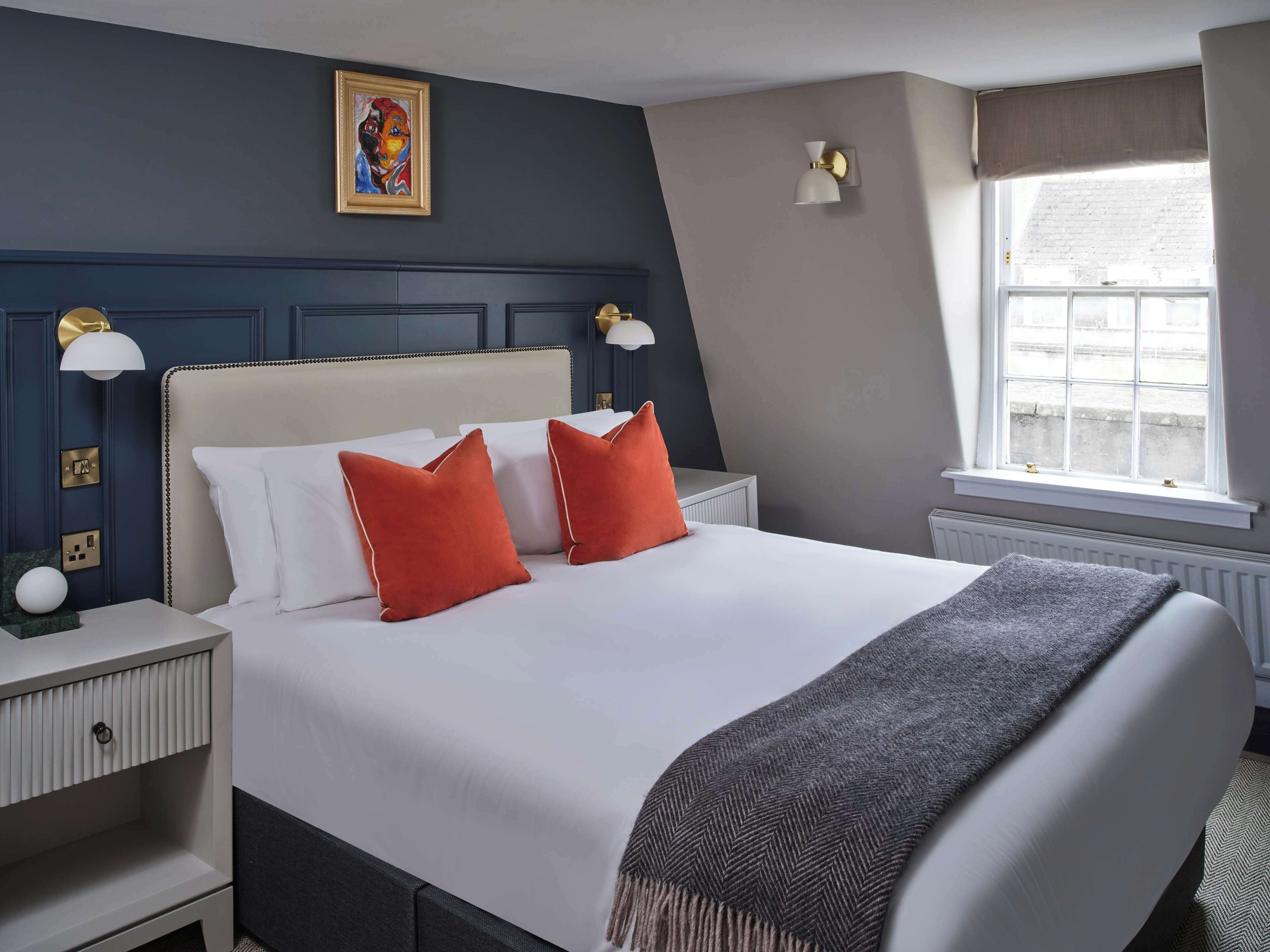 Ein Hotelzimmer mit einem großen Bett, zwei Nachttischen, einem Fenster mit Vorhängen und einem Bild an der Wand.