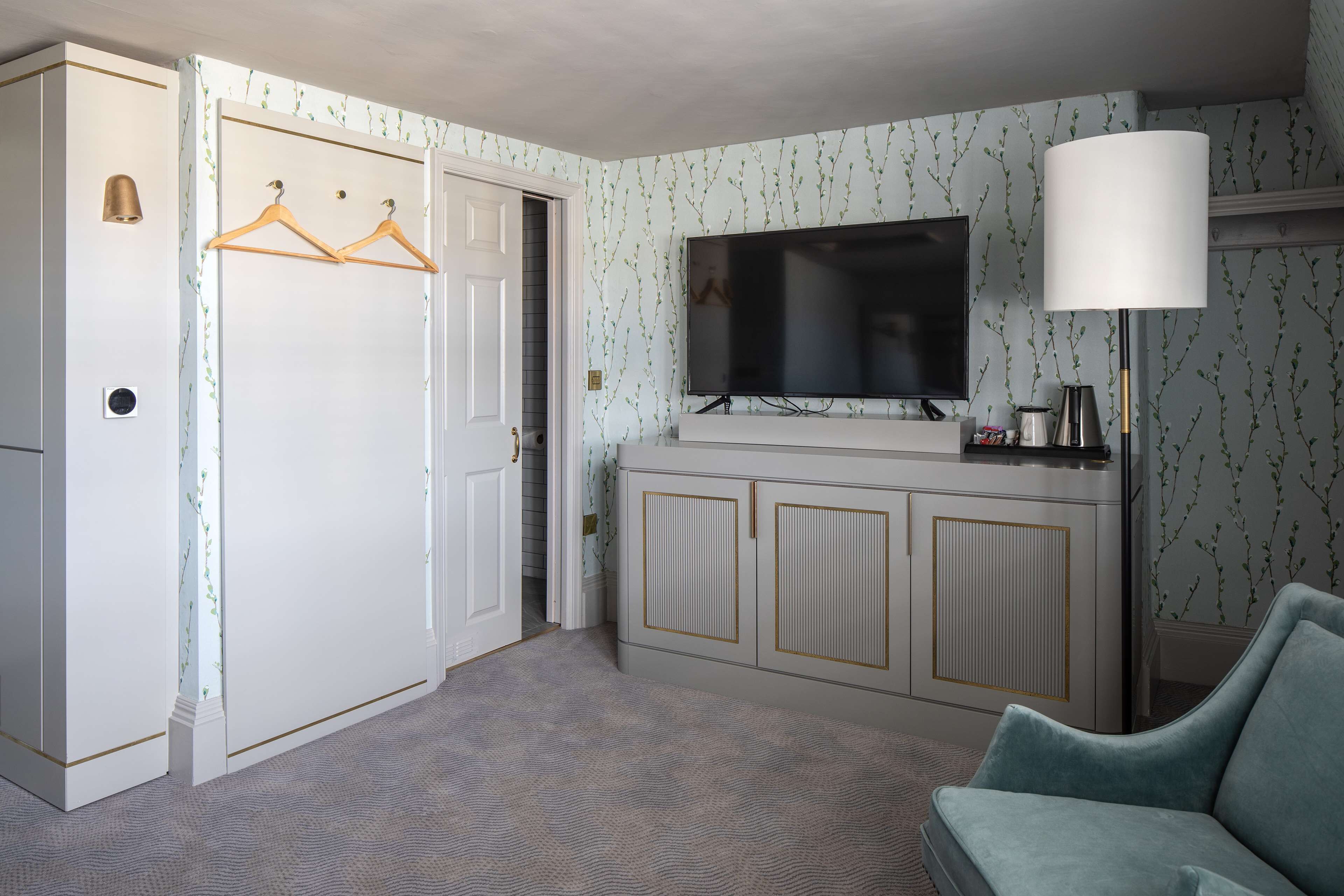 A hotel room with a TV, a sofa, a wardrobe, and a lamp.