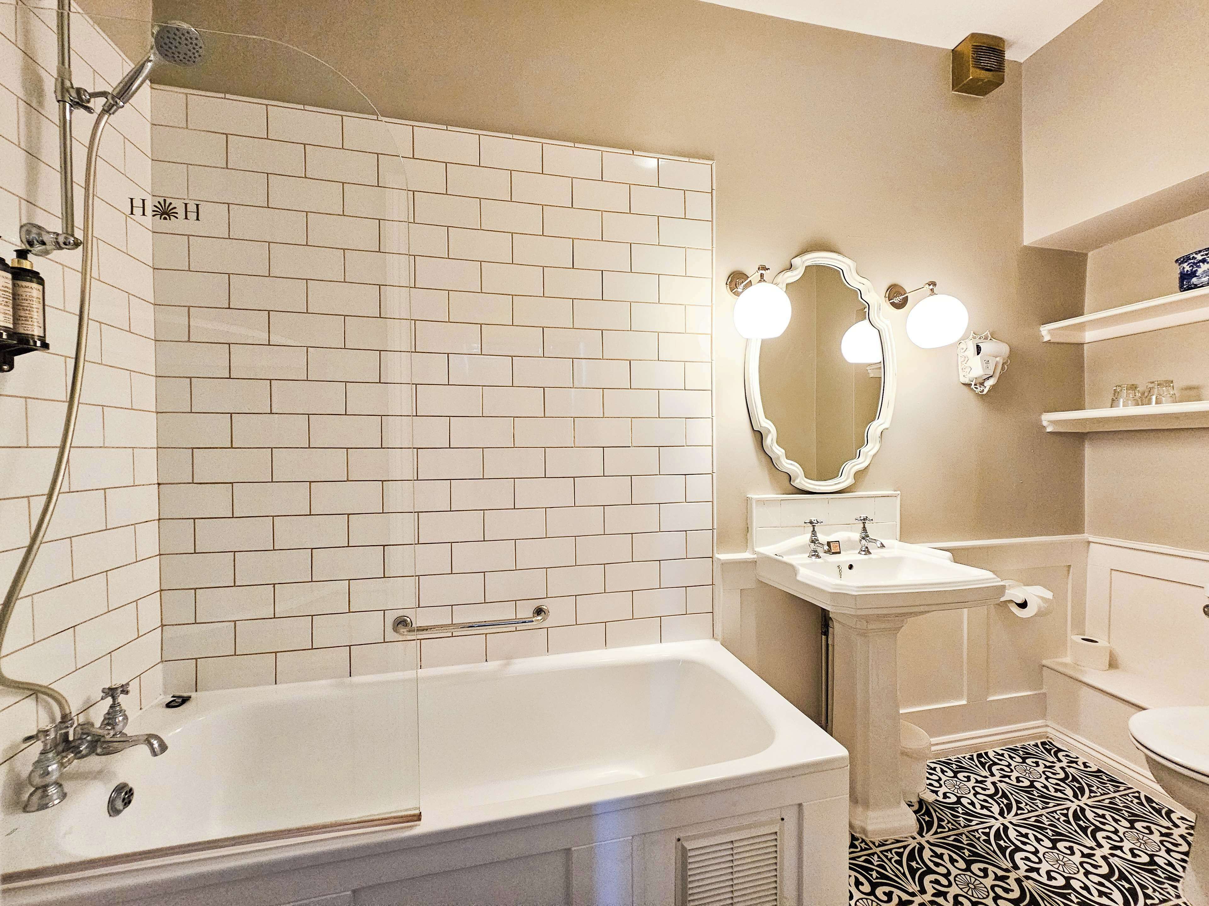 A bathroom with a white bathtub, a shower, a sink with a mirror, and a toilet.