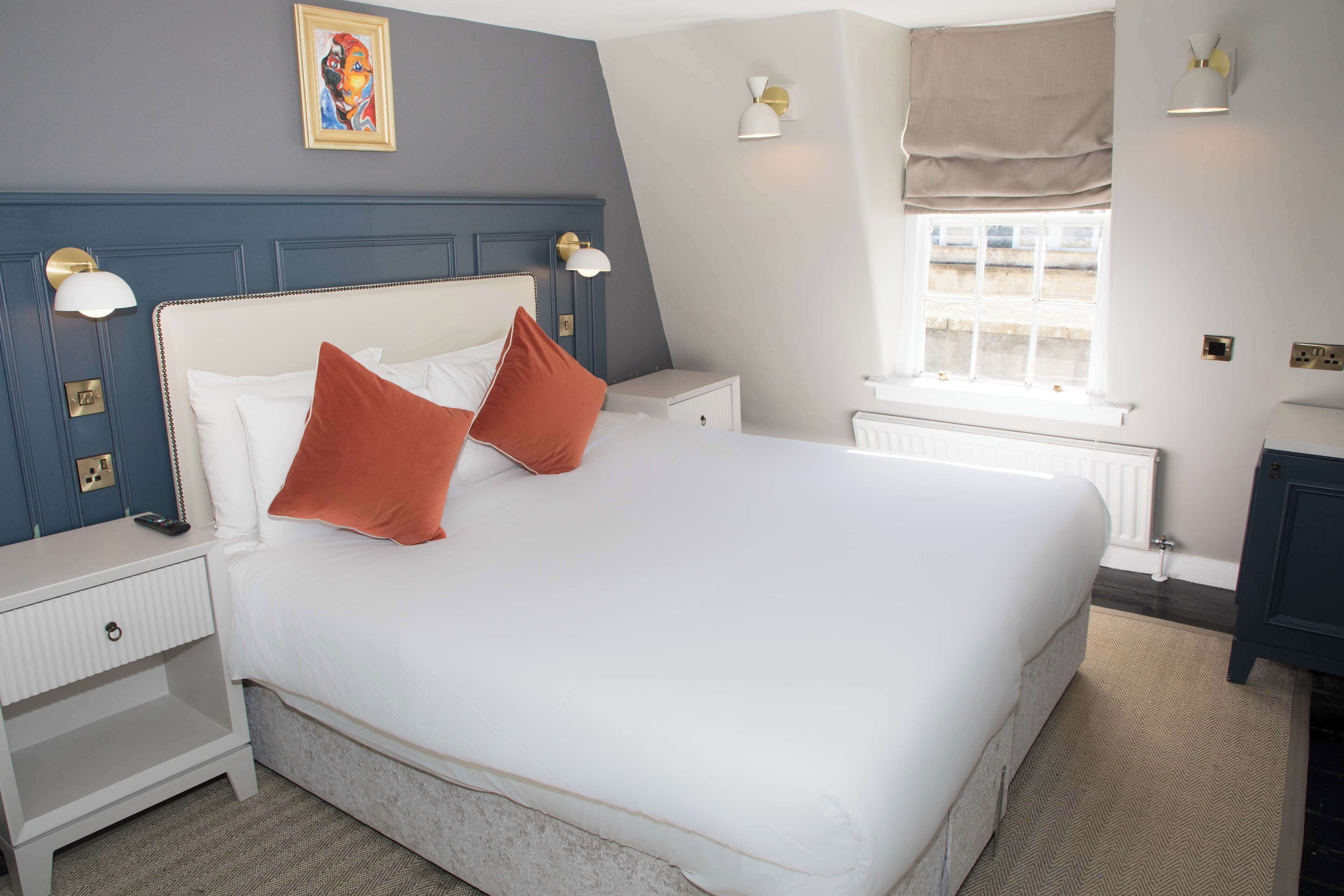 A neatly arranged bedroom with a large bed, bedside tables, a window with curtains, and wall-mounted lights.
